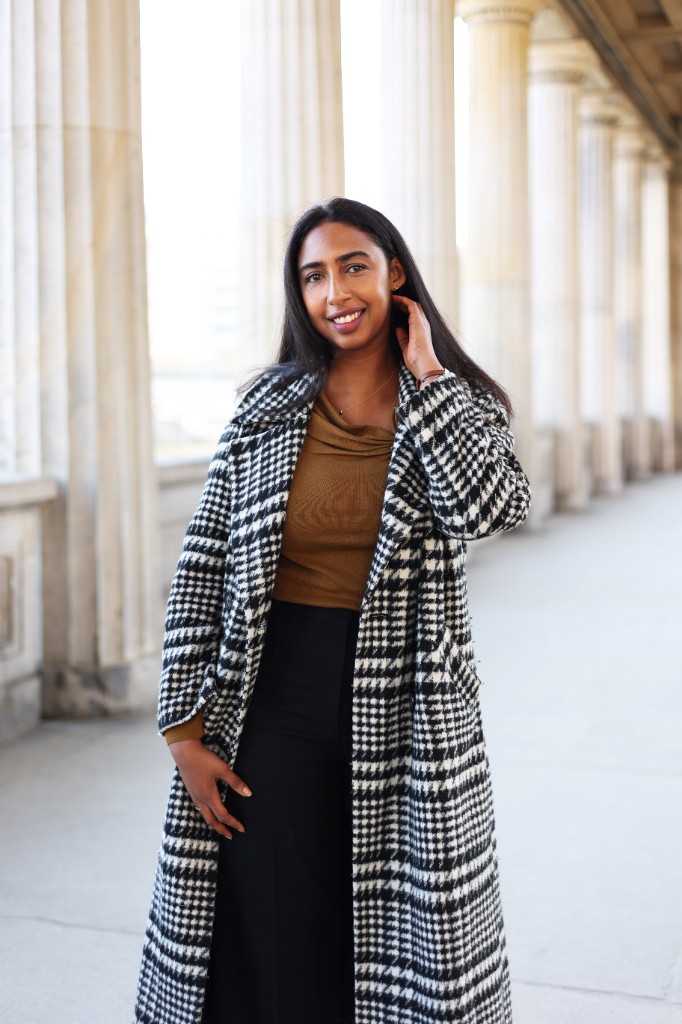 Sahra Malin, standing in a colonnade, wearing a houndstooth coat